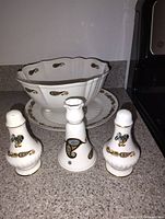 Photo showing the white glass bowl with scalloped edge, a matching large plate, and two small shakers all decorated with paisley designs.