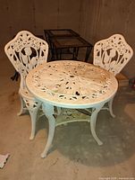Photo of white plastic patio set consisting of a round table and two matching chairs with ornate floral designs.