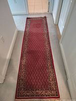 Full view of the red runner rug laid out in a hallway on light carpet
