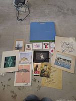 Wide shot of all items showing portfolio folder, loose prints, framed artworks and ephemera sheets laid out on the floor.