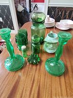 Overview of the vintage green glass lot including candlesticks, glasses, jars, clover dish, Phillips bottle and ceramic face mug