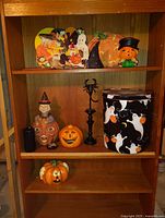 Photo showing vintage Halloween decorations arranged on a wooden shelving unit, including pumpkin and ghost-themed items, candle holders, and whimsical figurines