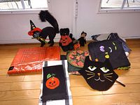 Full display of vintage Halloween items including large and small black plush cats in costume, Halloween-themed textiles, and decorative pieces arranged on wooden floor near windows.