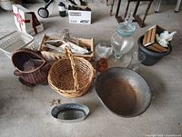 Multiple wicker baskets, glass vases, metal pan, and various decor items placed on a concrete floor.