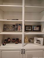 Wide shot of white shelves holding the vintage Christmas items, including framed art, ceramic church, decorative box, and small figurines.