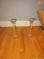 Pair of clear crystal candlesticks by Waterford on wooden floor against gray wall.