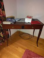 Wooden desk with curved legs and various items on top including cables, papers and decorative objects.