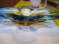 Side view of a thick, wavy art glass bowl with attractive light refraction and gradient colors in green, yellow, and amber hues.