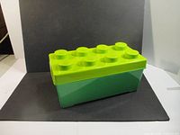 Closed green plastic storage container with yellow LEGO brick-style lid shown from side angle