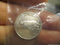 Reverse side of the Canadian Centennial 25-cent coin showing the walking cougar with inscriptions '25 CENTS', '1867-1967', and 'CANADA'. Coin is held in hand inside a plastic sleeve.