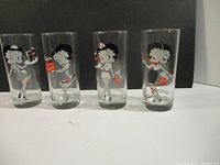 Front view of all four glasses in a row showing distinct Betty Boop Coca Cola designs