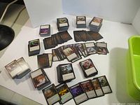 Multiple stacks and piles of Flesh and Blood trading cards arranged on a white table, showing front and back card faces, featuring artwork and game icons.