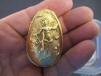 Close-up image showing the front of the pewter egg with raised angel motif, held in hand for scale.