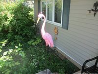 Front-right side view of the pink flamingo garden decoration in a garden setting showing its height and placement near a house.