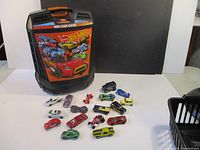 Image of Hot Wheels branded 100 Car Case standing upright with several die-cast cars laid out in front.