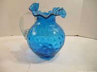 Front view of the blue glass pitcher showing ruffled edge and clear glass handle