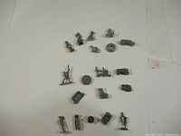 Overhead view of all metal Monopoly tokens laid out in rows on a white background showing various character designs, animals, and objects.