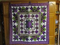 Full view of the handmade patchwork quilt hanging, showing the full square size and color pattern.