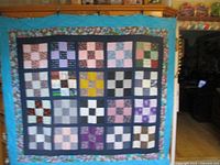 Full view of patchwork quilt laid flat showing all the patchwork squares, inner dark blue border, and floral outer border.
