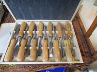 View of the entire set of 12 chisels neatly placed in a storage box with wooden handles and metal blades.