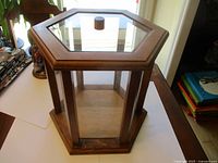 Wooden hexagonal showcase shown empty on a white surface, displayed indoors with visible light reflections on glass.