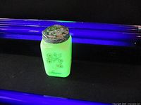 Uranium glass sugar shaker glowing green under UV light showing floral decoration and 'Sugar' label.