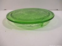 Side view showing the three feet of the green carnival glass cake plate with floral embossing.