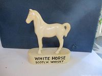 Front view of cream-colored ceramic horse figurine on oval base with text labeling.