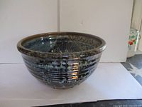 Glazed pottery bowl showing rounded shape and mottled dark blue and brown finish with exterior ridges.