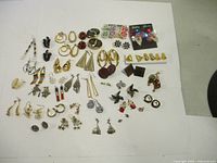 Full view showing an assortment of about 40 pairs of vintage earrings in different styles, sizes, and colors arranged on a white background.
