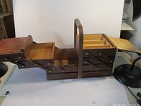 Folded out view of vintage wooden sewing box showing dark wood finish and multiple compartments, with the handle in the center.