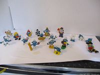 Lot of 18 vintage Smurf figures shown on white surface, various characters and accessories visible