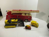 Four vintage Tonka toy trucks displayed on white background: large fire truck, bulldozer, dump truck, small forklift.