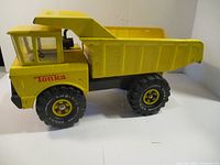 Side profile showing entire length of the yellow Tonka dump truck with clear windows and black wheels