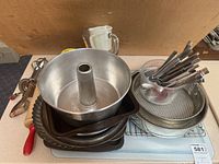 Image showing a variety of baking dishes including a bundt pan, tart pan, metal trays, a glass measuring cup with cutlery, and other kitchen utensils.