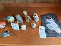 Group of nine bird and owl figurines with wall plaque partially visible