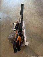 Top view of WORX cordless leaf blower with black and orange plastic body, long tube attachment and visible WORX branding.