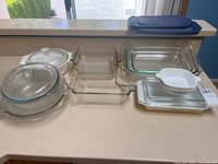Full overview of all glass and ceramic casserole dishes on countertop showing Pyrex and CorningWare pieces.