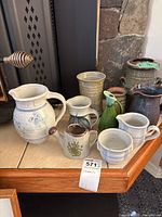 Full view of assortment on table edge showing 10 ceramic items including jugs, pitchers, vases, small watering can creamer, and sugar bowl.
