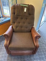 Front view of brown fabric and leather-like reclining chair, showing tufted backrest, fabric seat, and armrests.