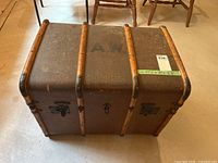 Top view of wooden trunk chest with 'A W' stenciling and measurement label taped to surface.