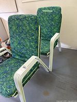 Two metal deck chairs with green leafy fabric cushions showing front-facing padded seats and backs