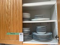 Ceramic bowls and plates with blue and gray striped and checkered patterns stacked inside a cabinet shelf