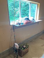 Wide view showing fishing rods standing against a wall, fishing net in a box, fishing line spools, and a hat on a windowsill.