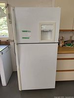 Front view of white GE refrigerator with freezer on top and fridge on bottom in a garage setting.