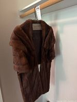 Brown mink fur stole hanging on a wooden hanger, showing the soft fur exterior.