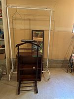 Full view of the metal garment rack, wooden shelf, mirror, and garment valet stand grouped together in a basement setting.