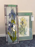 Two items side-by-side showing a tall rectangular stained glass panel with iris flowers and a framed floral print.