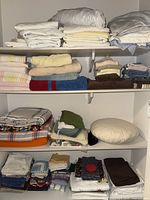 Photo of various folded bed linens, towels, table linens, and a pillow arranged on shelves