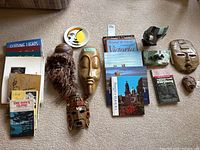 Overview photo showing all masks and books laid out on the floor, including wood, stone, and glass masks and assorted books about Victoria and Vancouver Island.